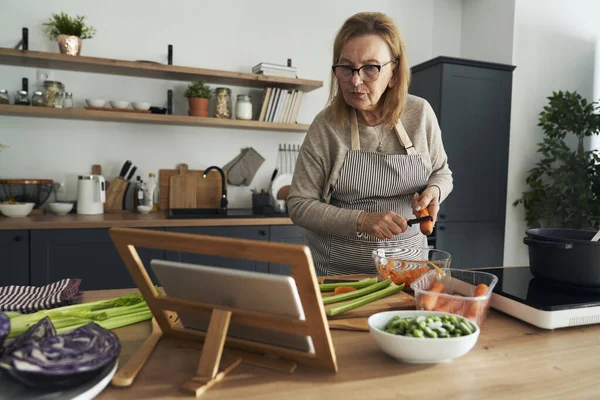Mulher Idosa Caucasiana Descascando Uma Cenoura Enquanto Cozinha Cozinha — Fotografia de Stock