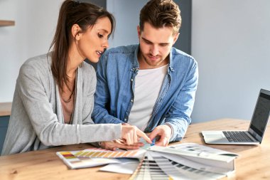 Beyaz çift mutfakta oturuyor ve yeni daire için renk seçiyorlar.