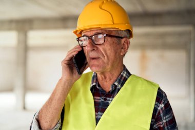 Kafkasyalı kıdemli mühendis inşaat alanında cep telefonuyla konuşuyor.