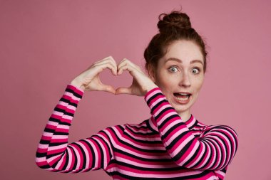 Elleriyle kalp şeklini gösteren genç bir kadının stüdyo fotoğrafı.                               