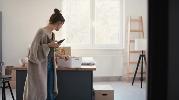 Young Caucasian Woman Using Mobile Phone While Unpacking Stuff New — Stock Video