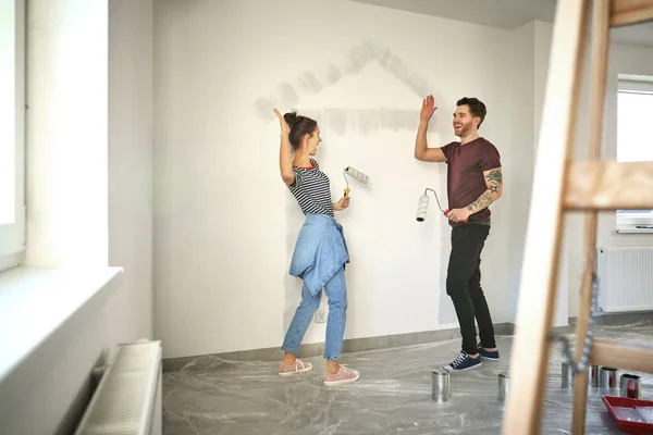 年轻的高加索夫妇在新房子的墙上涂满了房子的形状后 给了他们高达五块 — 图库照片