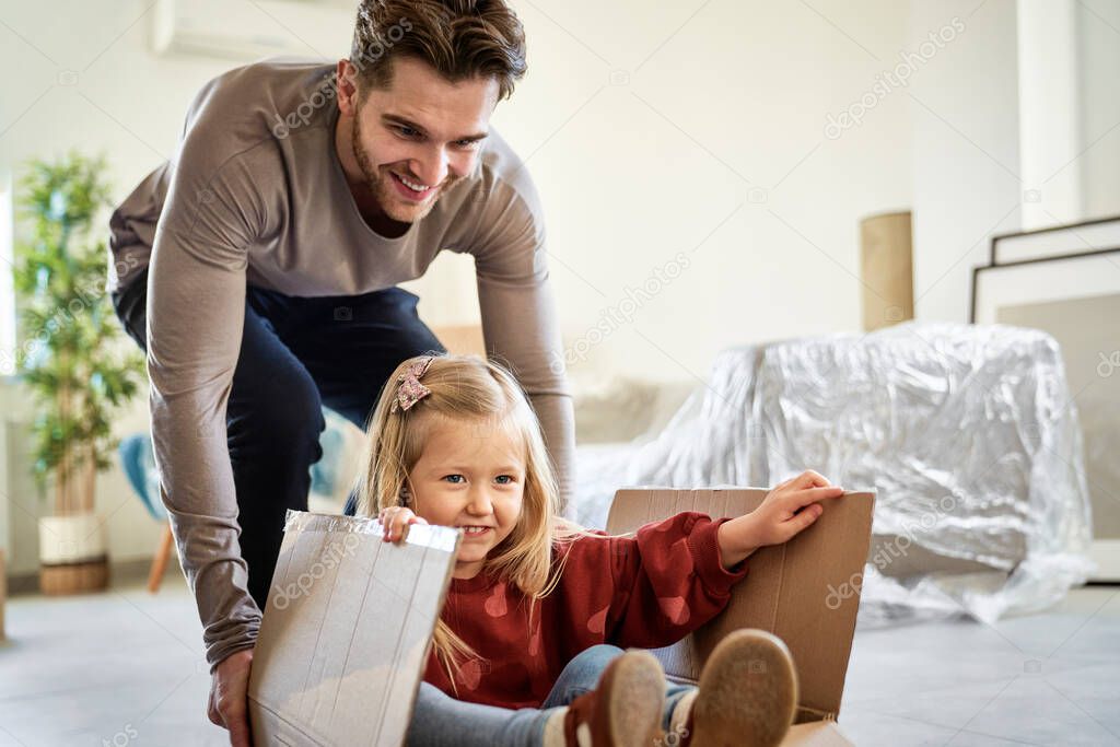 Caucasian father pushing little girl in paper box while moving house 