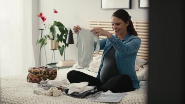 Kaukasiska Kvinna Avancerad Graviditet Sitter Sängen Och Vikbar Baby Kläder — Stockvideo