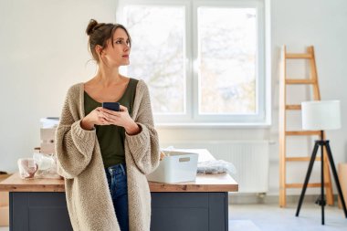 Yeni evde eşyaları yerleştirirken cep telefonu kullanan beyaz bir kadın.