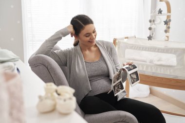 Hamileliği ilerlemiş beyaz bir kadın bebek odasında ultrason taraması yapıyor.