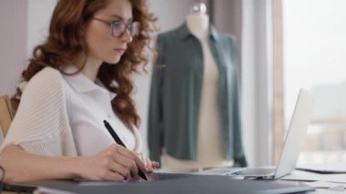 Kızıl yetişkin kadın iş yerinde dizüstü bilgisayar ve dijital tablet kullanıyor. 8K 'da kırmızı helyum kamerayla çekildi.   
