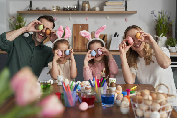 Portrait of playful caucasian family covering eyes with easter eggs and laughing