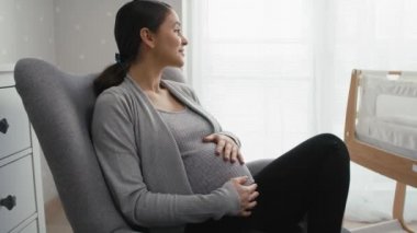 İlerlemiş hamilelik döneminde beyaz bir kadının koltuğa oturup karnını okşamasını yakınlaştır. 8K 'da kırmızı helyum kamerayla çekildi..