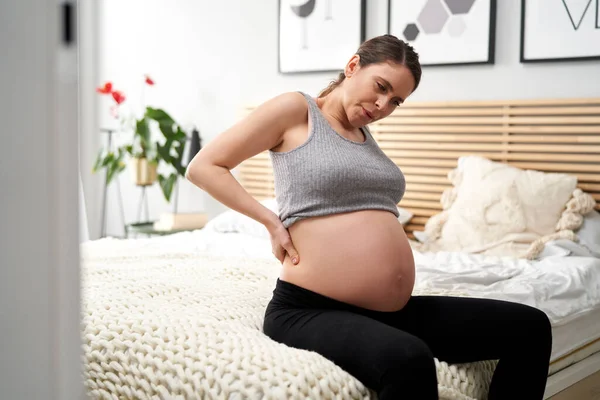 怀孕晚期的白种人妇女坐在床上 背痛难忍 — 图库照片