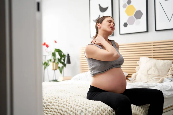 怀孕晚期的白人妇女坐在床上 感到脖子剧痛 — 图库照片