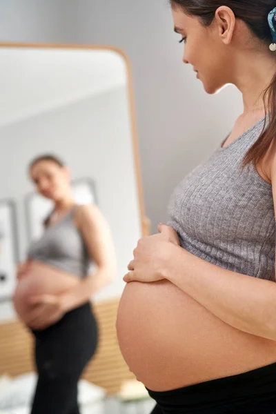 鏡の中で自分自身を閲覧高度な妊娠中の白人女性の垂直画像 — ストック写真