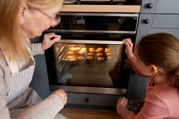 白人奶奶和孙女在烤箱里检查饼干 — 图库照片