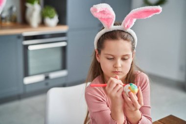 Ev mutfağında paskalya yumurtası dekore eden beyaz bir kız. 