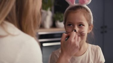 Kafkas anne ve kızı kızın yüzüne Paskalya tavşanı çiziyor. 8K 'da kırmızı helyum kamerayla çekildi.   