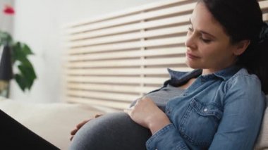 Hamileliği ilerlemiş beyaz bir kadın yatakta dinleniyor. 8K 'da kırmızı helyum kamerayla çekildi..