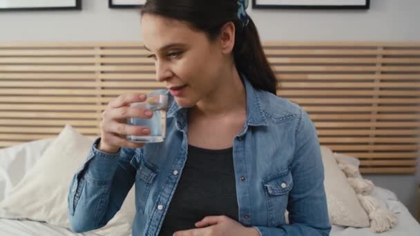 先進妊娠中の白人女性の正面図は ベッドの上に座って水を飲む 8Kでレッドヘリウムカメラで撮影 — ストック動画
