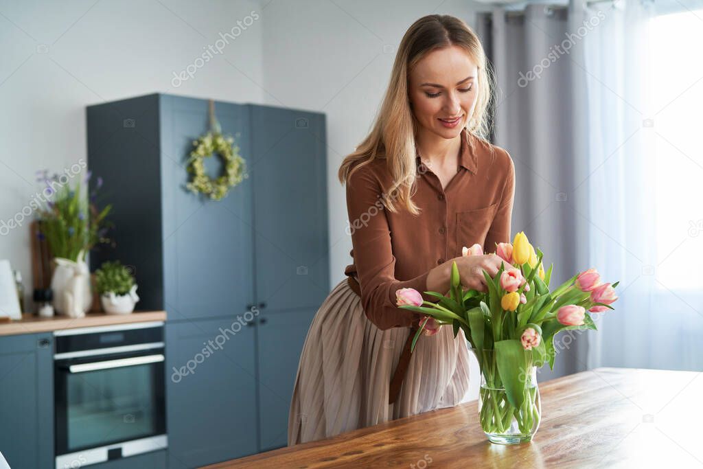 Caucasian woman putting fresh tulips into the vase in the home kitchen