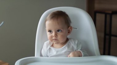 Yüksek sandalyede yemek bekleyen küçük bir kızın videosu. 8K 'da kırmızı helyum kamerayla çekildi.. 