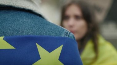 AB ve Ukrayna bayraklarıyla kaplı kadın ve erkek yüz yüze duruyor ve konuşuyor. 8K 'da kırmızı helyum kamerayla çekildi.. 