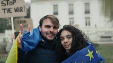 Avrupa Birliği ve Ukrayna bayraklarıyla kaplanmış beyaz erkek ve kadın barış işareti gösteriyor. 8K 'da kırmızı helyum kamerayla çekildi..   