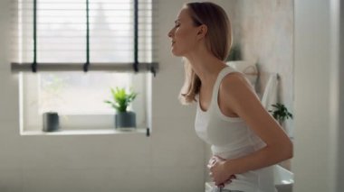 Genç beyaz kadın banyoda duruyor ve midesinde ağrı hissediyor. 8K 'da kırmızı helyum kamerayla çekildi..  