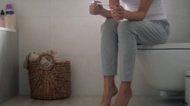 Stresli, tanınmayan bir kadın tuvalette oturup hamilelik testi sonuçlarını bekliyor. 8K 'da kırmızı helyum kamerayla çekildi.. 