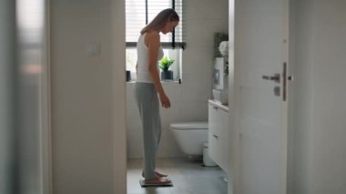 Hüsrana uğramış beyaz kadın banyo terazisine basıyor. 8K 'da kırmızı helyum kamerayla çekildi..   