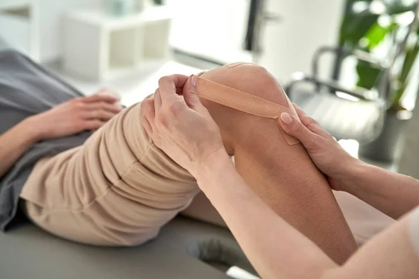 Physical therapist applying kinesio tape to the patient\'s knee