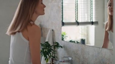 Beyaz bir kadının evdeki banyoya gelip aynaya baktığının videosunu izliyorum. 8K 'da kırmızı helyum kamerayla çekildi.. 