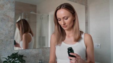 Genç beyaz kadın banyoda hap alıyor. 8K 'da kırmızı helyum kamerayla çekildi..   