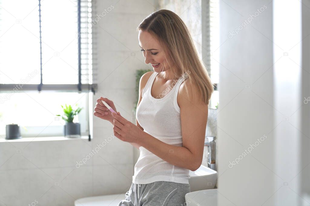 Cheerful woman standing and holding a pregnancy test 