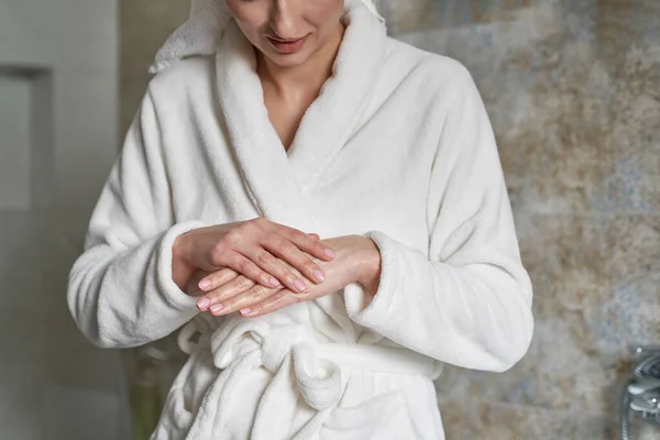 无法辨认的妇女在浴衣上用保湿霜在手上 — 图库照片