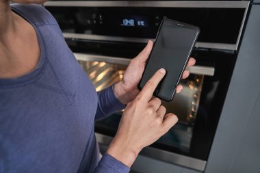 Cep telefonu tutan kadına yaklaş ve evde fırını aç. 
