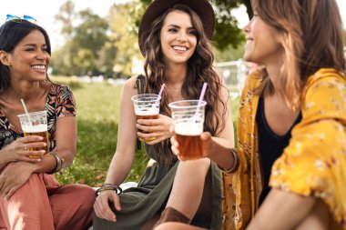 Üç kadın çimenlerde oturup bira içiyor.
