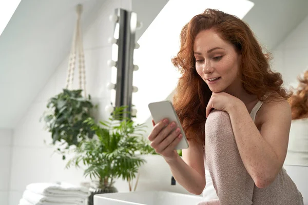 Smiling Caucasian Woman Sitting Bathroom Using Mobile Phone — Fotografia de Stock