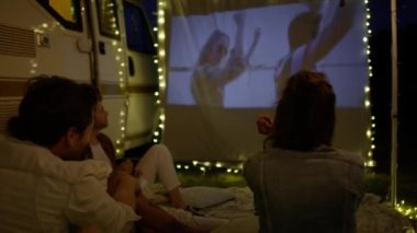 Kamp alanında projeksiyon ekranında film izleyen bir grup neşeli genç. 8K 'da kırmızı helyum kamerayla çekildi.  