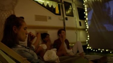 Kamp alanında projeksiyon ekranında film izleyen bir grup neşeli genç. 8K 'da kırmızı helyum kamerayla çekildi.  