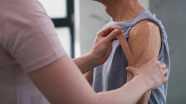 Physical therapist applying kinesio tape on senior patient's arm. Shot with RED helium camera in 8K.  