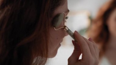 Gülümseyen beyaz kadın banyoda yüz silindiri kullanıyor. 8K 'da kırmızı helyum kamerayla çekildi.. 