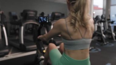 Back view of woman exercising on rowing machine. Shot with RED helium camera in 8K. 
