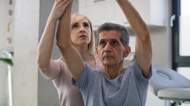 Doktorun ofisinde kıdemli bir adamla çalışan kadın fizyoterapist. 8K 'da kırmızı helyum kamerayla çekildi..    