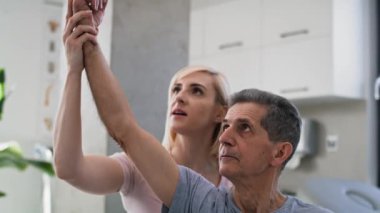 Yaşlı adamın kolunu esneten kadın fizyoterapist. 8K 'da kırmızı helyum kamerayla çekildi..   