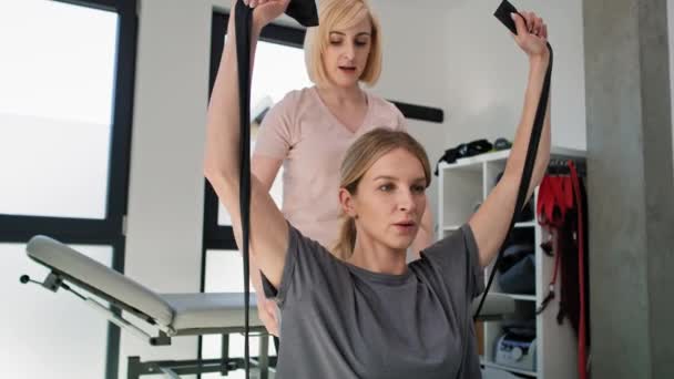 Fisioterapeuta Feminina Trabalhando Com Mulher Jovem Usando Goma Exercício Tiro — Vídeo de Stock