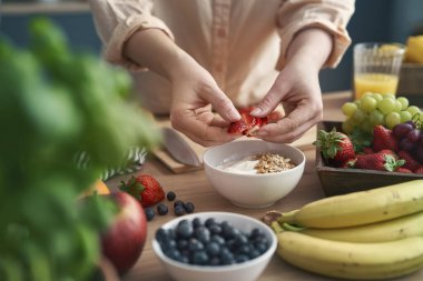 Woman making bowl full of yogurt with strawberries 