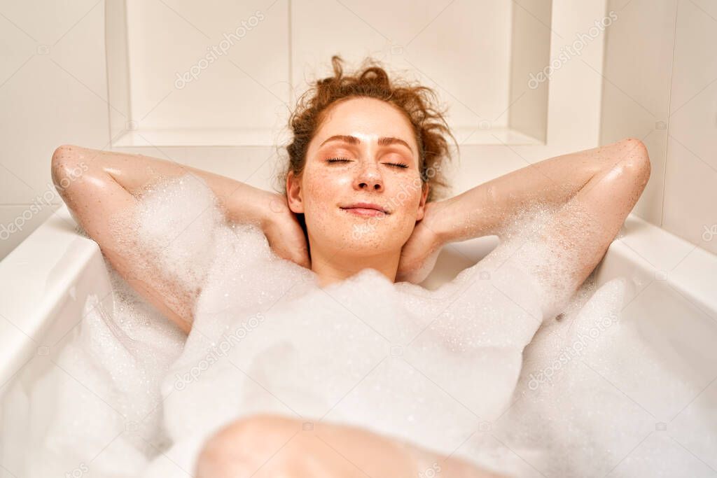 Young redhead woman taking a bath with eyes closed 