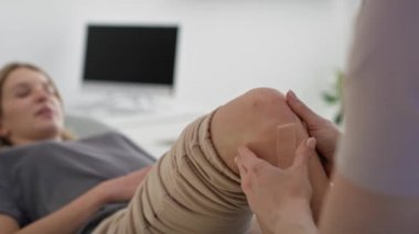Fizyoterapist hastanın dizine Kinesio bandı yapıştırıyor. 8K 'da kırmızı helyum kamerayla çekildi..   