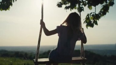 Arkadan bakan sarışın kız yaz gününde yüksekte sallanıyor. 