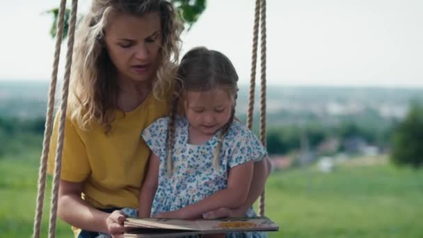 Mamá Con Niña Balanceándose Leyendo Libro Día Verano — Vídeos de Stock