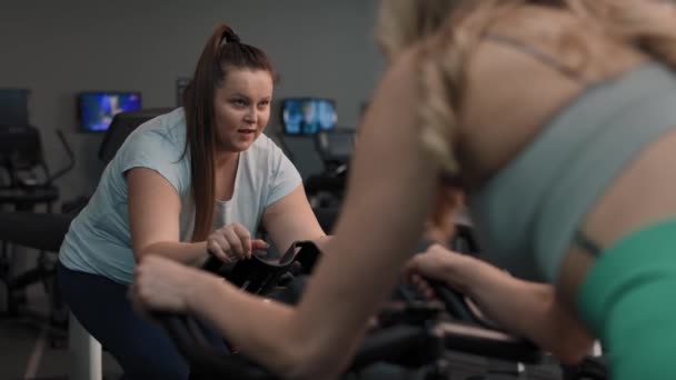 Two Caucasian Women Ride Bikes Gym Shot Red Helium Camera — Stock Video